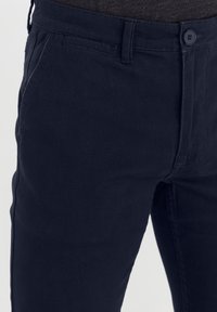 Mørk marineblå chinos laget av bomullsstoff, med knappelukking, frontlommer og en glatt tekstur. Tilpasset passform med minimalistisk design.