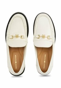 Witte leren loafers met een gouden accentketting, gestructureerde zwarte rubberen zool en tonale stiksels. Het interieur heeft geperforeerde details voor ademend vermogen.