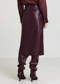 Jupe midi en cuir bordeaux avec une taille cintrée, une fente au dos et une texture lisse, associée à des bottes en cuir assorties à talons hauts et froncées.