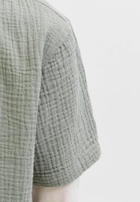 Close-up of a light gray textured fabric sleeve with a quilted grid pattern on a white background.