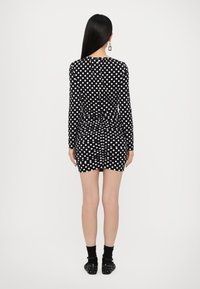 Black long-sleeve dress with white polka dots, fitted design, ruched detailing at the back, paired with black socks and studded shoes.