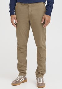 Tan bomullschinos med slim fit, med en midja av medelhöjd och standardfickor, i kombination med grå sneakers och vita snören.