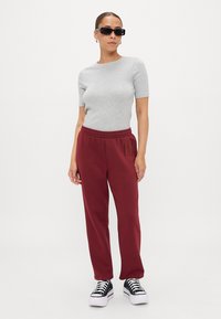 Maglietta grigia a maniche corte, pantaloni della tuta bordeaux con vita elasticizzata e scarpe da ginnastica nere con suole bianche. Gli occhiali da sole completano il look.