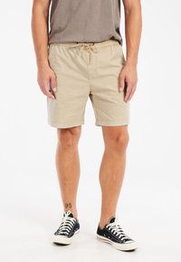 Beige katoenen shorts met een elastische tailleband en trekkoord, zijzakken en omgeslagen zoom. Draag ze met zwarte canvas sneakers.