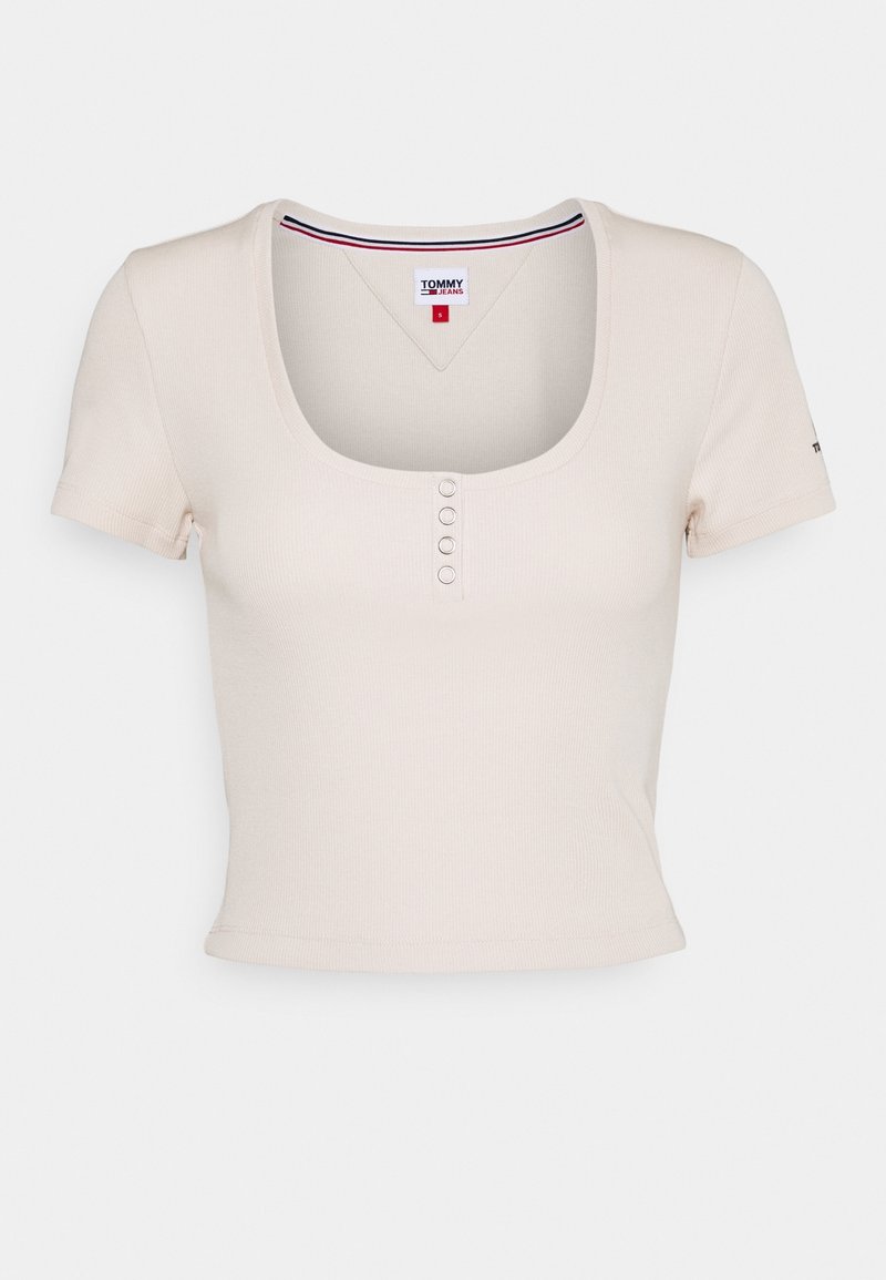 Crop top côtelé crème à manches courtes avec encolure ronde et quatre petits boutons sous le col, étiqueté Tommy Jeans taille small.