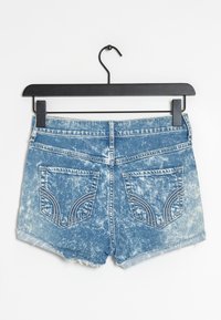 Džínové kraťasy se světlemodrou vybledlou barvou, třepeným lemem a dvěma zadními kapsami s dekorativním prošíváním. Zavěšené na černém ramínku.