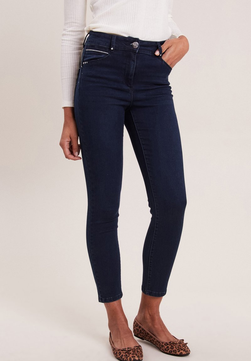 Jeans skinny in denim blu scuro con vita alta, tasche frontali e una vestibilità aderente, dotati di una texture elegante e di un design minimalista.