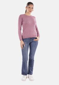 Maglione lungo a maniche lunghe di colore lilla con scollo rotondo, abbinato a jeans flare blu e sneakers bianche. Design semplice senza pattern.