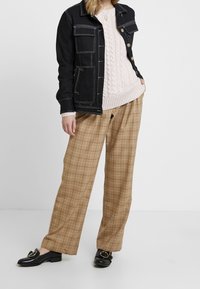 Svart denimjacka med vit sömnad, ljusrosa kabelstickad tröja, beige rutiga byxor och svarta loafers med gulddetalj i form av spänne.