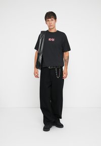 Sorte oversized t-skjorte med rødt AC/DC-logo, kombinert med vide svarte bukser, svart belte med kjededetaljer, og svart skulderveske.