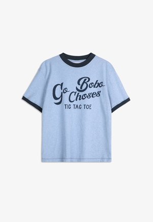 Světle modré bavlněné tričko s černým žebrovaným kulatým výstřihem. Na přední straně se nachází černý text "Go Bobo Choses Tic Tac Toe" v různých písmových stylech. Krátké rukávy.