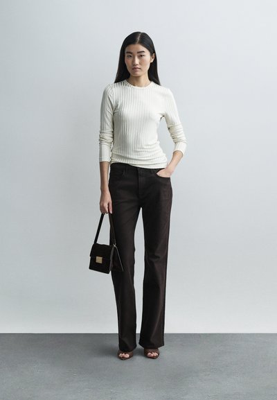 Kremasta dolgo rokavna majica z rebrastim vzorcem, združena s temno rjavimi hlačami s ravnimi nogavicami. Model drži majhno rjavo semišasto torbico z zlato kovinsko opremo.