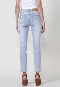 Vaqueros de denim azul claro con forma ajustada, que cuentan con bolsillos traseros y un parche de marca de cuero marrón en la cinturilla.