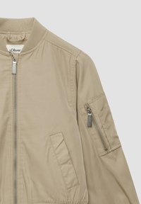 Veste bomber beige avec un col côtelé, fermeture éclair à l'avant et poches latérales. Dispose d'une poche zippée supplémentaire sur la manche.