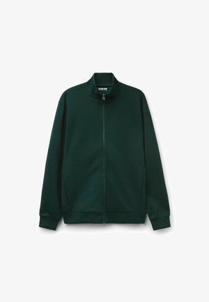 Veste zippée vert foncé avec un col haut, fabriquée en tissu doux. Dispose de manches longues et de poches latérales. Design simple et épuré.