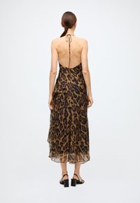 Robe midi à imprimé léopard avec fines bretelles, dos nu et tissu fluide et léger. Présente une texture à plusieurs couches et un ourlet superposé.