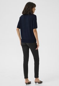 Mörkblå kortärmad stickad topp med rundad halsringning och ribbad trim, tillsammans med slim-fit svarta jeans och lågklackade svarta mule-skor.
