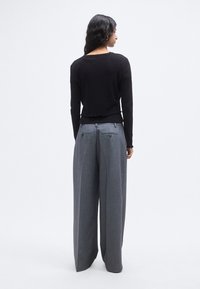 Μαύρο πλεκτό τοπ με μακρύ μανίκι και κυματιστή ραφή στο τελείωμα, συνδυασμένο με ψηλόμεσο, φαρδύ γκρι παντελόνι με φερμουάρ στις πίσω τσέπες.