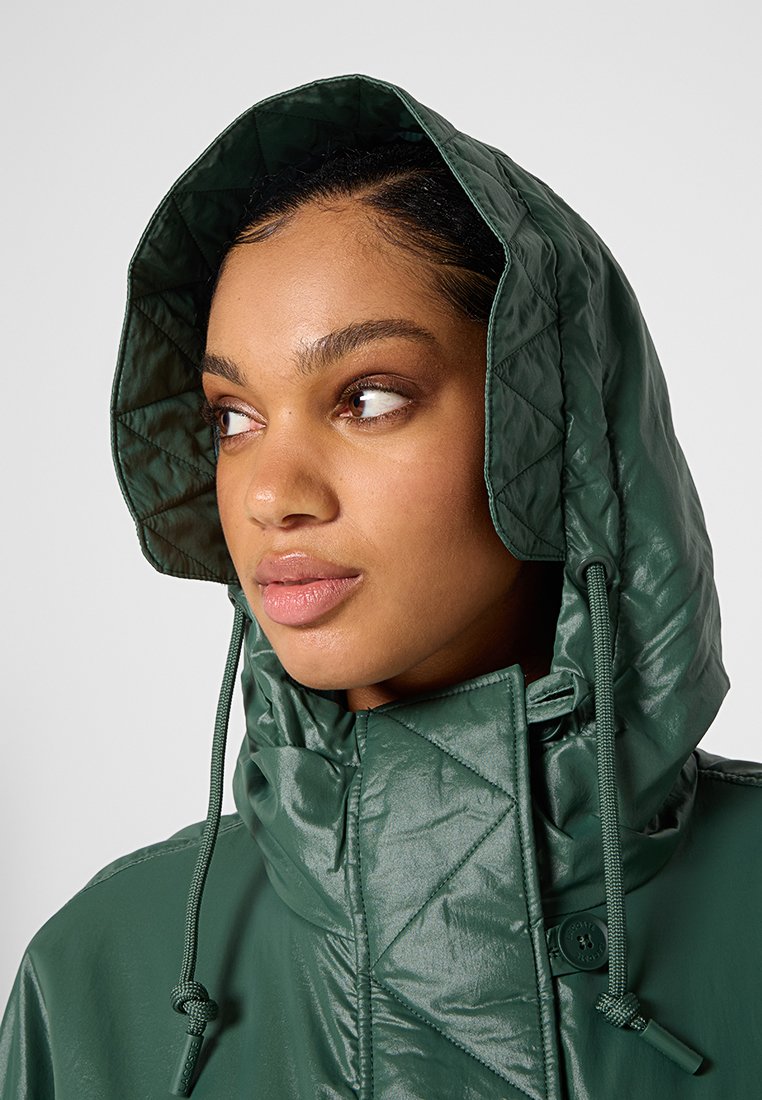 Chaqueta verde acolchada con cuello alto y capucha. Presenta cuerdas ajustables, textura suave y un acabado brillante.