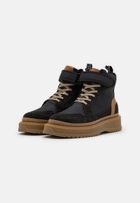 Zapatillas altas con un upper de tela y ante negro con acentos beige, cordones beige y una suela de goma gruesa. Presentan dos tiradores.
