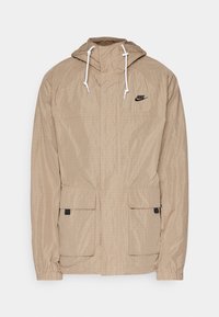 Beige lättviktsjacka med en strukturerad yta, justerbar huva och vita snören. Har två frampocket och en liten svart logotyp.