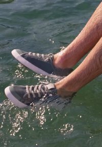 Jambes portant des baskets grises éclaboussant dans de l'eau claire, avec la lumière du soleil se reflétant à la surface de l'eau.