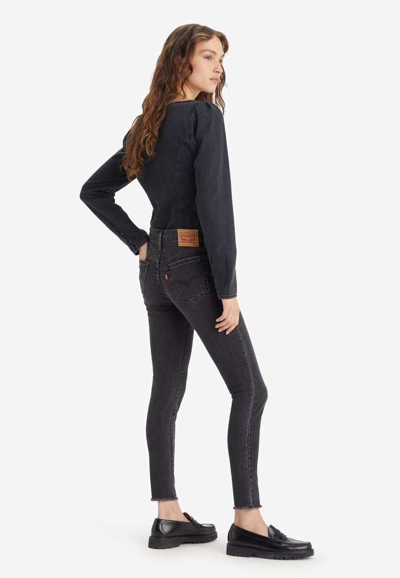 Jean skinny noir en denim avec une taille haute, un ourlet effiloché et une étiquette en cuir de marque. Associé à un haut ajusté à manches longues et des mocassins noirs.