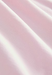 Světlé růžové plátno s hladkým, mírně texturovaným povrchem, které vykazuje jemné záhyby a vrásky v materiálu.