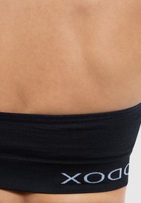 Zwarte elastische tailleband met ribbeltextuur, met witte logo-details, tegen een gladde, gebruinde huid.