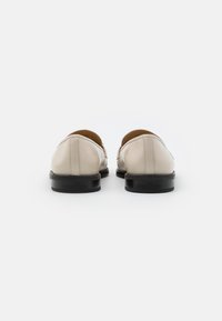 Mocassins en cuir beige à texture lisse, forme arrondie et semelles en caoutchouc noires. Présentent des accents de couture discrets au niveau des talons.