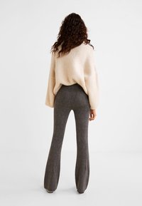 Cream oversized knit sweater paired with dark gray flared trousers. The sweater features a textured finish; pants have a smooth, tailored look.