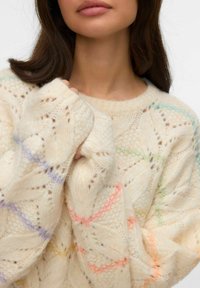 Maglione spesso lavorato a maglia color crema con motivo in pizzo. Presenta accenti colorati in tonalità pastello di rosa, giallo, verde e blu.