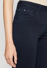 Mörkblå denimjeans med smal passform och lätt stretch. Funktionen inkluderar en sidficka med röd, vit och blå accent på bakre delen.