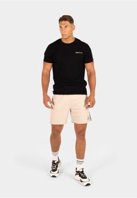 Zwarte crewneck t-shirt met een klein logo, gecombineerd met lichtbeige shorts met een gestructureerd patroon en zijbranding. Schoeisel is zwart en wit.