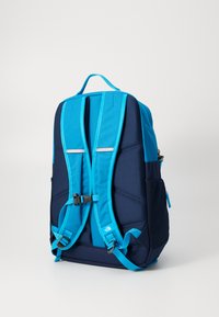 Un sac à dos bleu et marine avec des bretelles rembourrées, des poches latérales en maille, des accents réfléchissants et une solide poignée supérieure. Le tissu texturé ajoute de la durabilité.