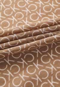 Tessuto marrone con un motivo di logo bianco ripetuto, con una texture liscia e strati piegati che mettono in risalto il design.