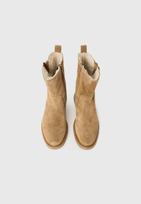 Beige Wildleder-Ankle-Boots mit einem weichen Innenfutter, seitlichem Reißverschluss und runder Zehenpartie. Die Sohle ist flach und strukturiert für besseren Grip.
