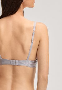 Soutien-gorge gris à rayures avec bretelles ajustables et fermeture à crochets. Texture douce semblable à du satin visible au dos, avec un détail de sangle portant la marque.