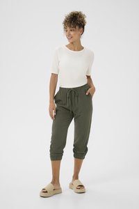 Hvid ribbet kortærmet top, olivengrøn linnedbuks med elastiske manchetter og snøre, parret med beige vævede slip-on sandaler.