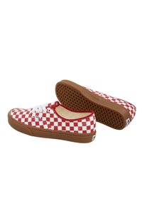 Baskets slip-on à carreaux rouges et blancs avec semelle en caoutchouc, lacets blancs et semelle externe en cuir texturé marron. Présente le logo Vans sur le côté.