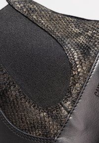 Calzado negro con una parte superior texturizada de aspecto serpentino, panel elástico y acentos de cuero suave, con un acabado mate.