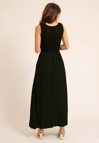 Robe maxi noire avec un corsage en dentelle texturée, taille cintrée et jupe fluide. Dotée d'un col rond et de talons à lanières.