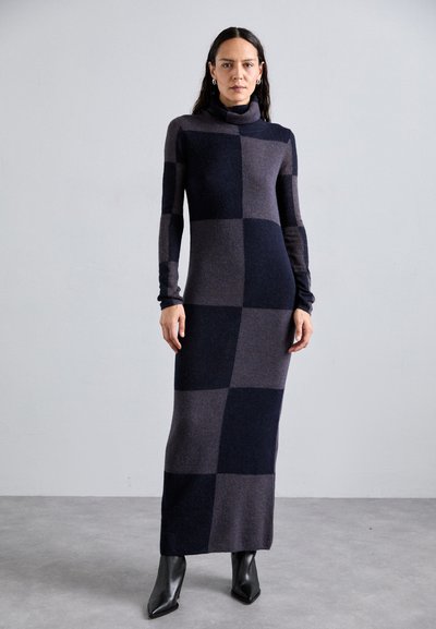 Rochie cu mâneci lungi, ajustată, în model de tablă de șah bleumarin și gri. Material tricotat moale cu guler înalt și siluetă subțire. Purtați cu botine negre cu toc.