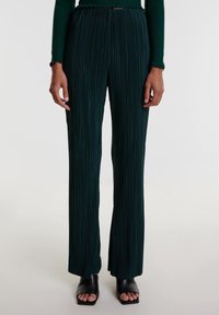 Groene geplooide broek met uitlopende benen, textiel met structuur, hoge taille en een gladde afwerking. Gecombineerd met zwarte blokhak sandalen met open tenen.