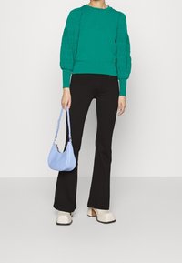 Teal trui met getextureerde pofmouwen, zwarte flarebroek, crèmekleurige platform schoenen en een lichtblauwe handtas. Glad materiaal en getailleerd ontwerp.