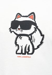 Κινούμενης εικόνας λευκή γάτα με πορτοκαλί αυτιά και μύτη σε σχήμα καρδιάς, φορώντας υπερμεγέθη μαύρα γυαλιά ηλίου, με το κείμενο "KARL LAGERFELD" από κάτω.