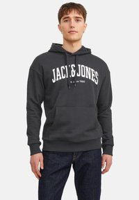Dunkelgrauer Hoodie mit weißem "JACK & JONES"-Text, Kängurutasche, verstellbarem Kordelzug, gerippten Bündchen und Saum; kombiniert mit dunkelblauen Jeans.