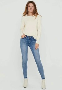 Krämfärgad stickad tröja, blå skinny jeans och vita ankelstövletter. Enkel design med en avslappnad passform, mjuk textur och klassiska färger.