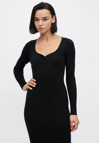 Μαύρο πλεκτό φόρεμα με ριγέ υφή, στρογγυλή λαιμόκοψη, μακριά μανίκια και κουμπιά μπροστά. Εφαρμοστή γραμμή, υφή με ανάγλυφα σχέδια.