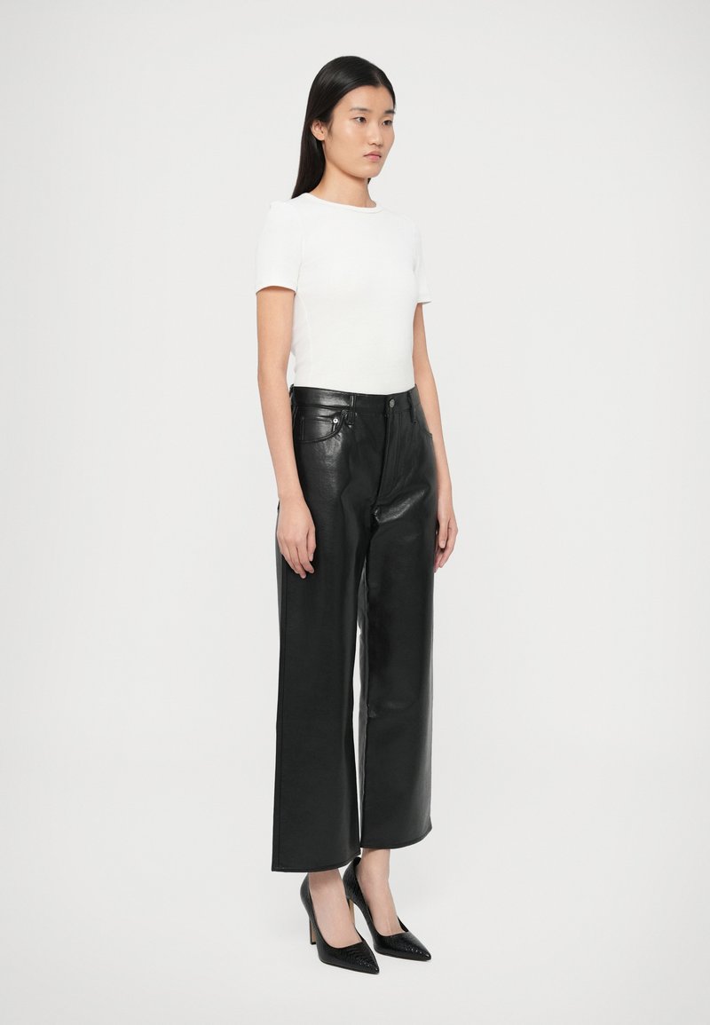 Top bianco a maniche corte abbinato a pantaloni in pelle nera a vita alta, con design a gamba dritta. Completa il look un paio di décolleté nere con punta a stiletto.